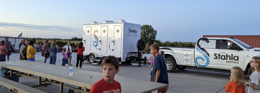 Image 2: Outdoor event with portable restrooms and pickup truck.