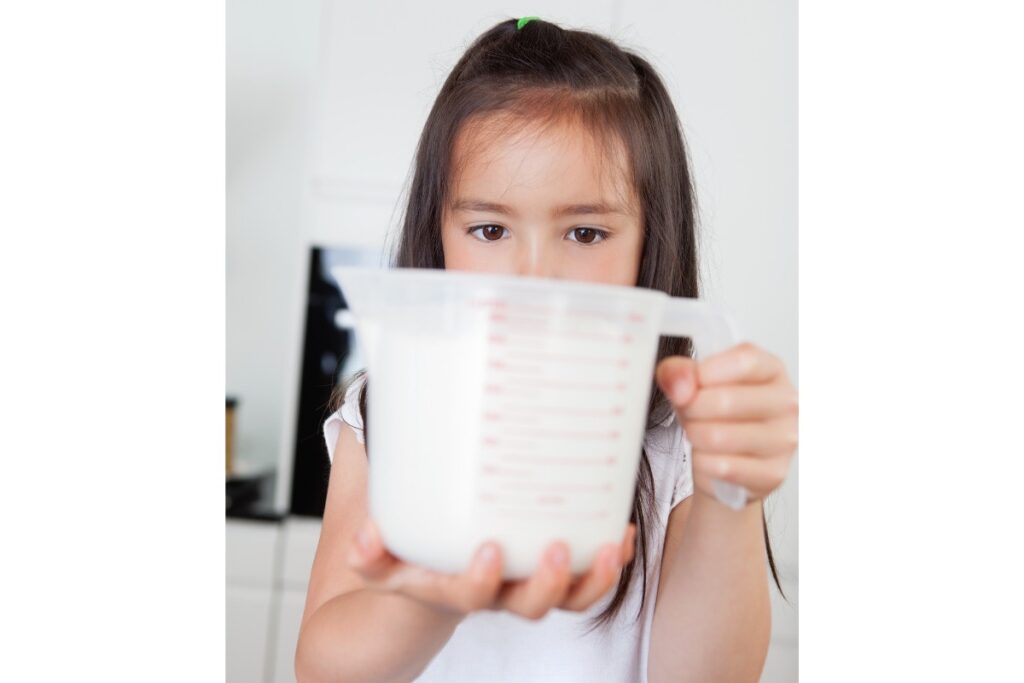 Girl holding measuring cup with milk.