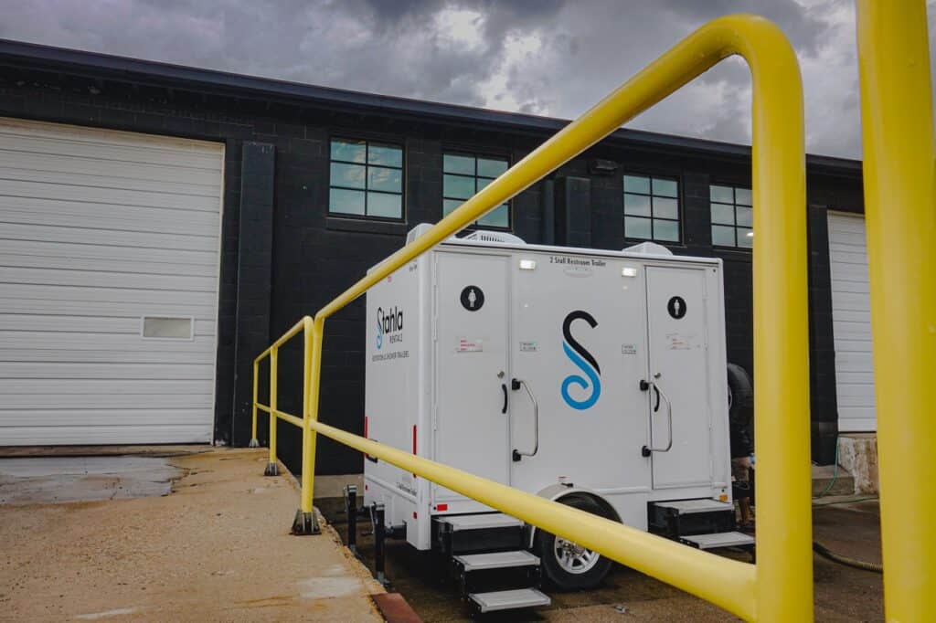 a white trailer labeled "solo by onvi" is parked outside a black industrial building with two large white roll up doors, courtesy of stahla services. yellow railings line the path leading to the trailer.