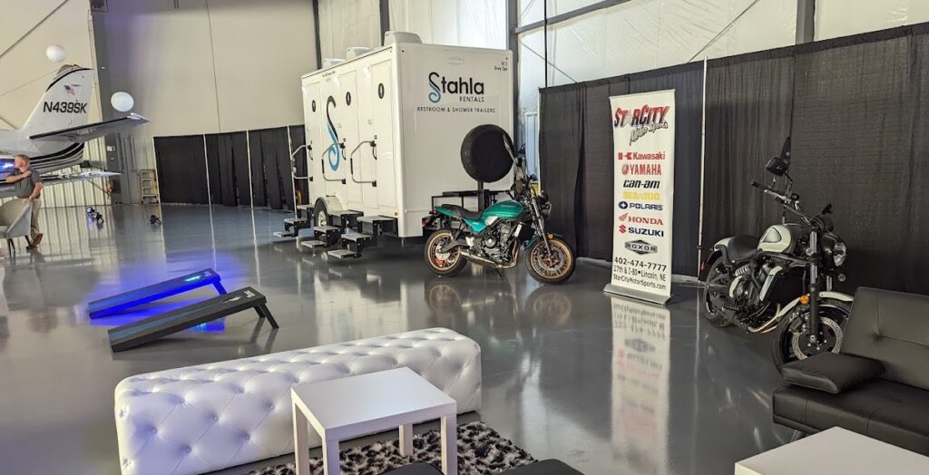 Exhibition hall with motorcycles, plane, and luxury restroom trailer.