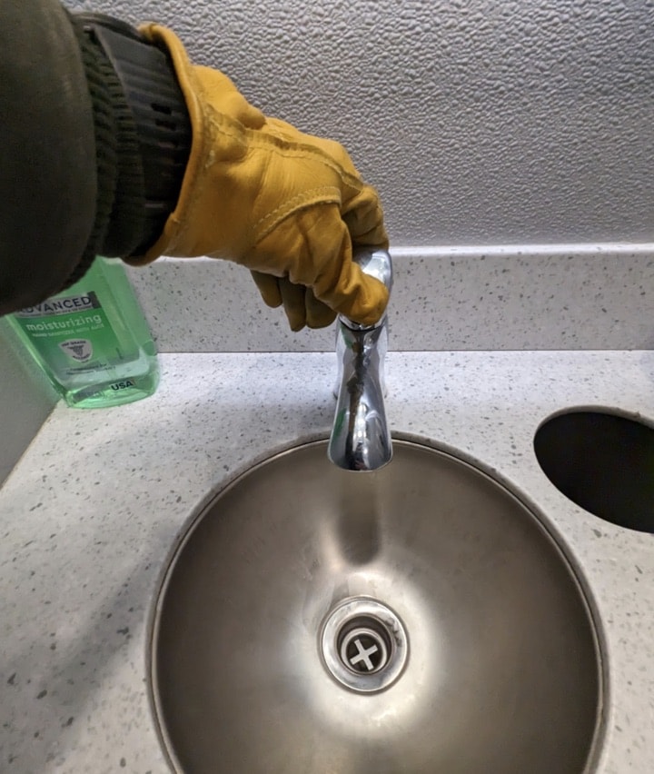 Person in glove adjusting sink faucet.