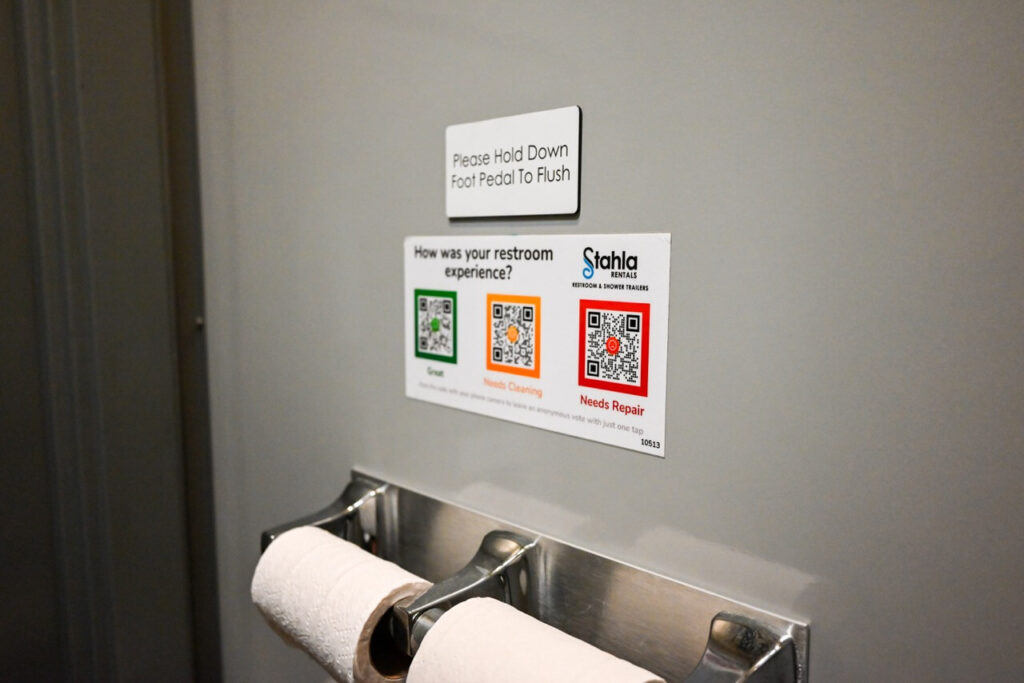 restroom feedback sign above toilet paper dispensers with qr codes for "great," "needs cleaning," and "needs repair" enhances the attendee experience at the nsaa state track event. also, remember to hold down the foot pedal to flush in our restroom trailers.