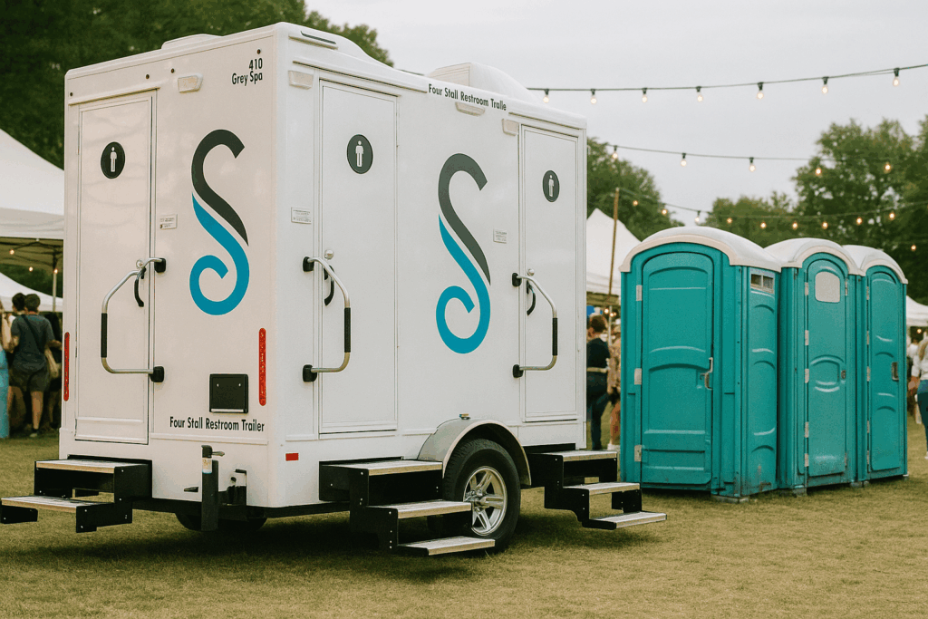 A premium restroom trailer and three portable toilets are set up on grass at an outdoor event, with people, tents, and string lights visible in the background—ideal for peak season planning or summer 2026 festivities.