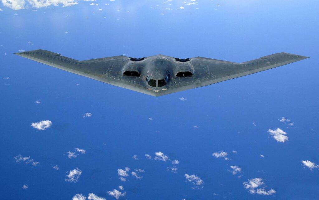 A black stealth bomber aircraft in flight above a blue sky with scattered clouds, serving as a powerful military tribute to advanced aviation technology.