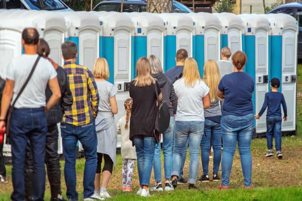People waiting in line for portable toilets outdoors.