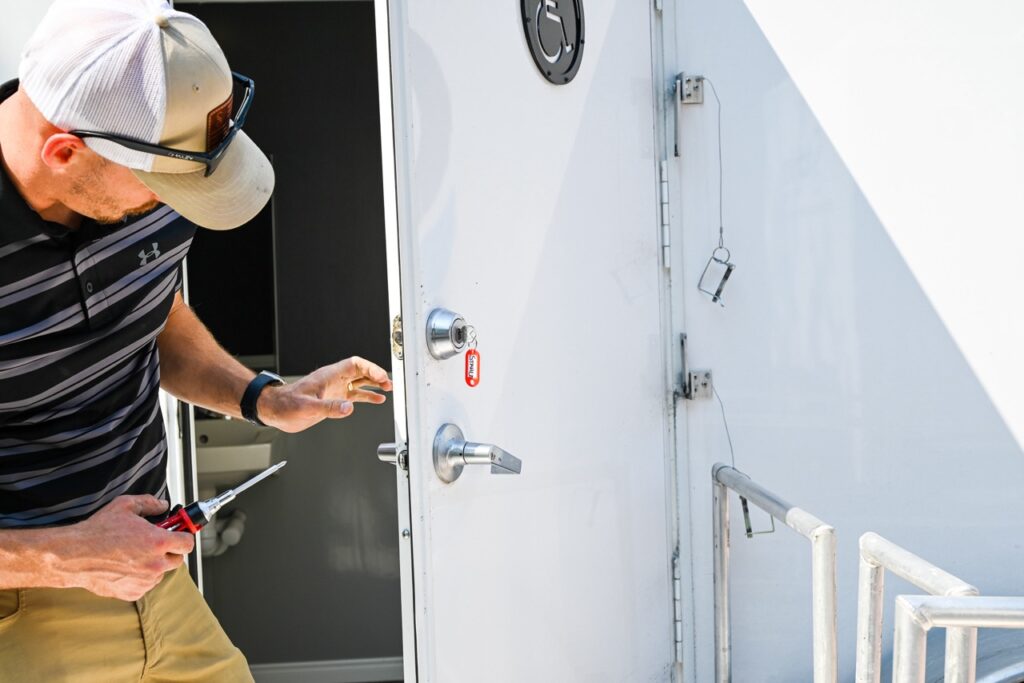 a person in a striped shirt and cap, embodying the comfort and tradition of the orange city tulip festival, uses a screwdriver on the lock of a white door.