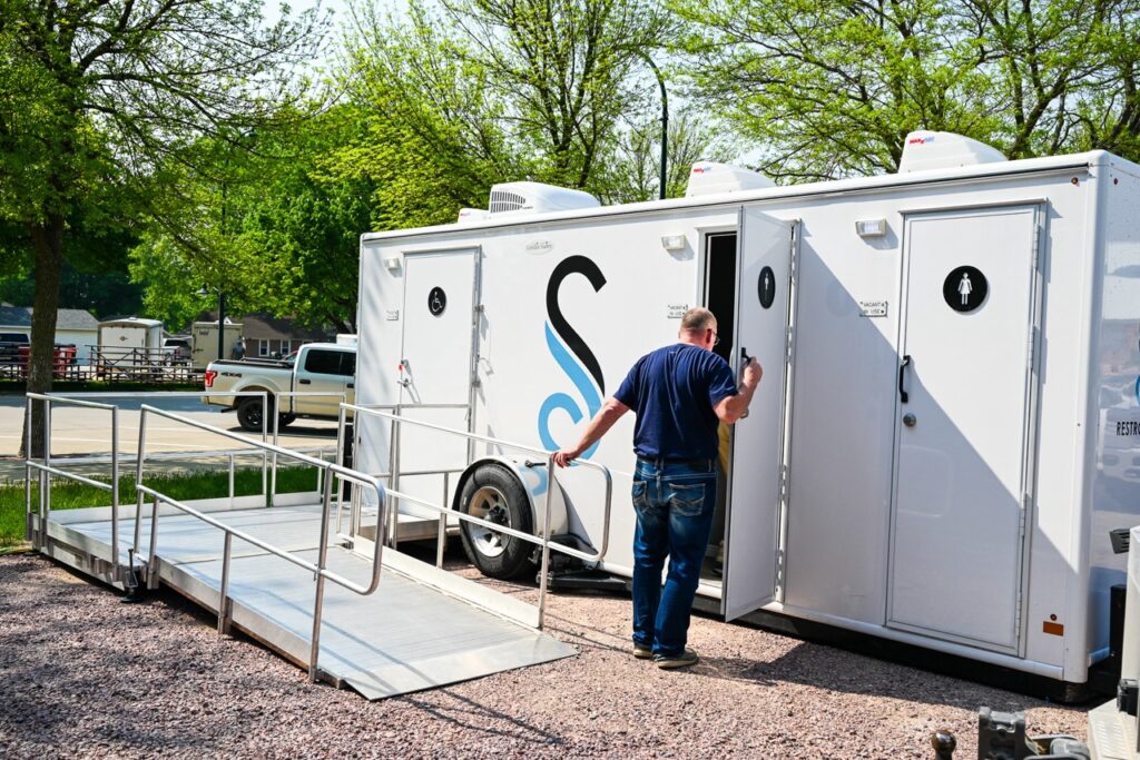at the orange city tulip festival, a man enters a stahla restroom trailer equipped with a convenient ramp, nestled in an outdoor, park like setting.