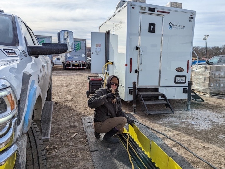 Person squatting near trucks and mobile service trailer.
