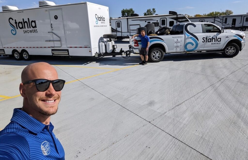 Man smiling with company vehicles and trailer.