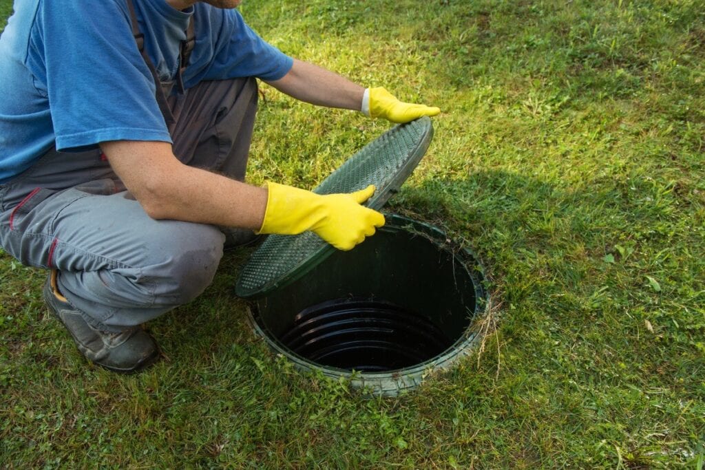 Man inspecting sewage system access on lawn.