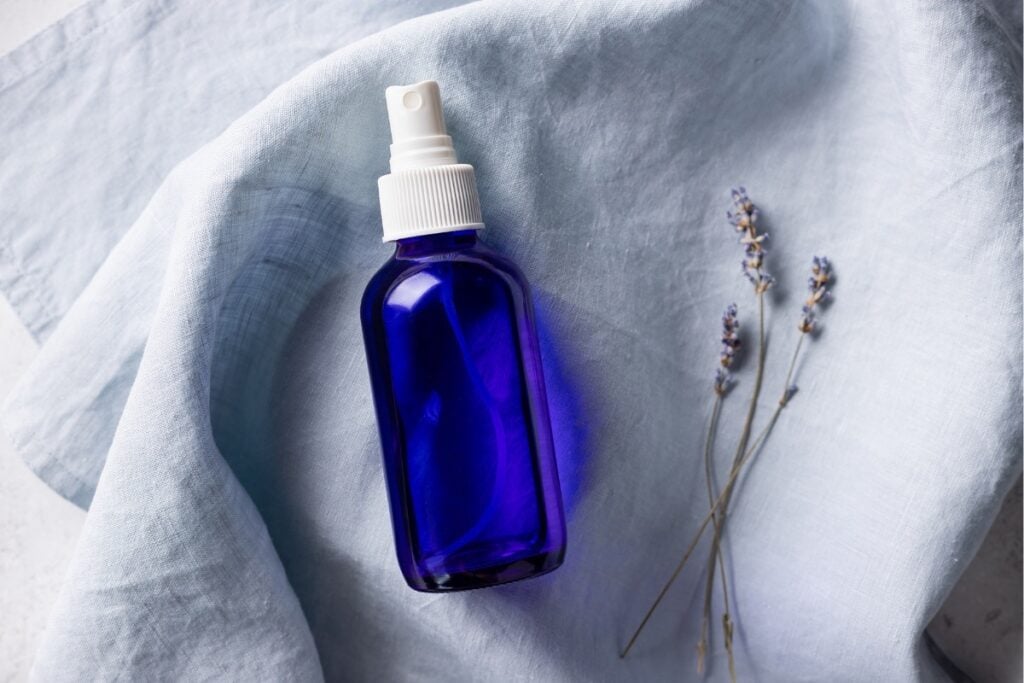 Blue glass spray bottle with lavender on linen.
