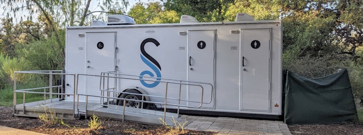 Image 8: Outdoor portable restroom trailer in natural setting.