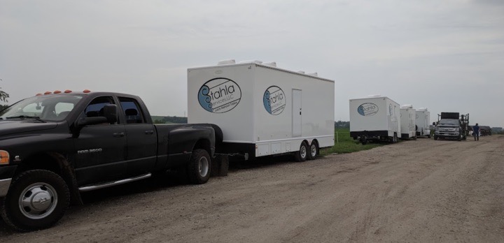 Trucks towing white trailers on a dirt road.