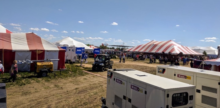Outdoor festival with tents, people, and generators.