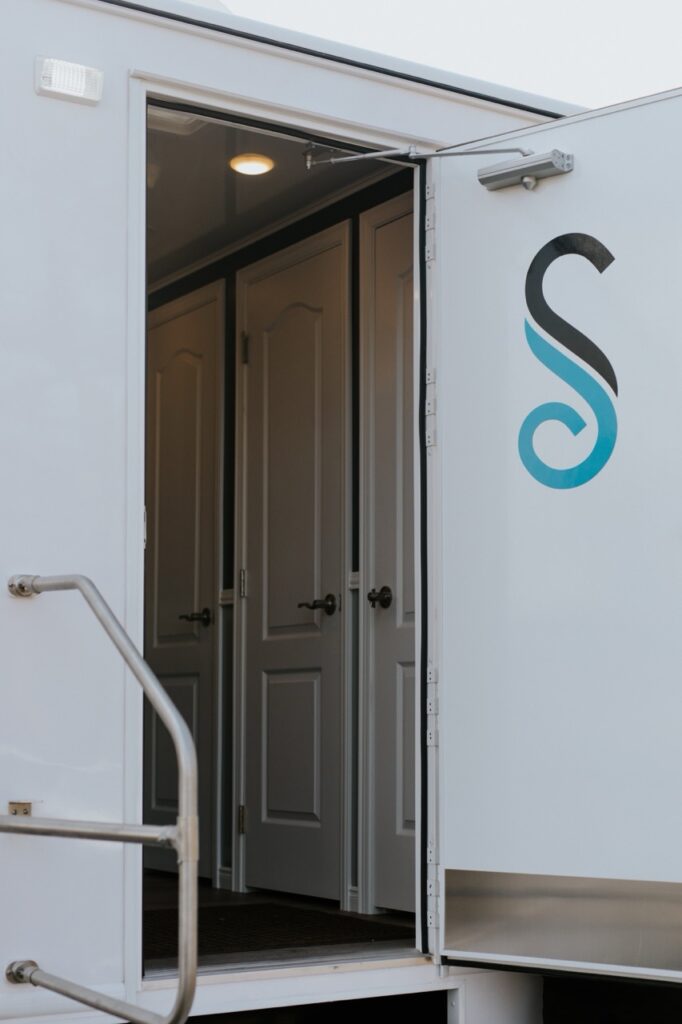 Open door of a white trailer showing multiple interior doors; a stylized 's' logo is visible on the exterior, ready to enhance your guest experience for the grand opening.