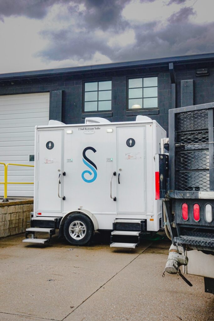a mobile sanitation trailer from stahla services, boasting two doors, is parked outside a building near a garage door at the red bull distribution company.