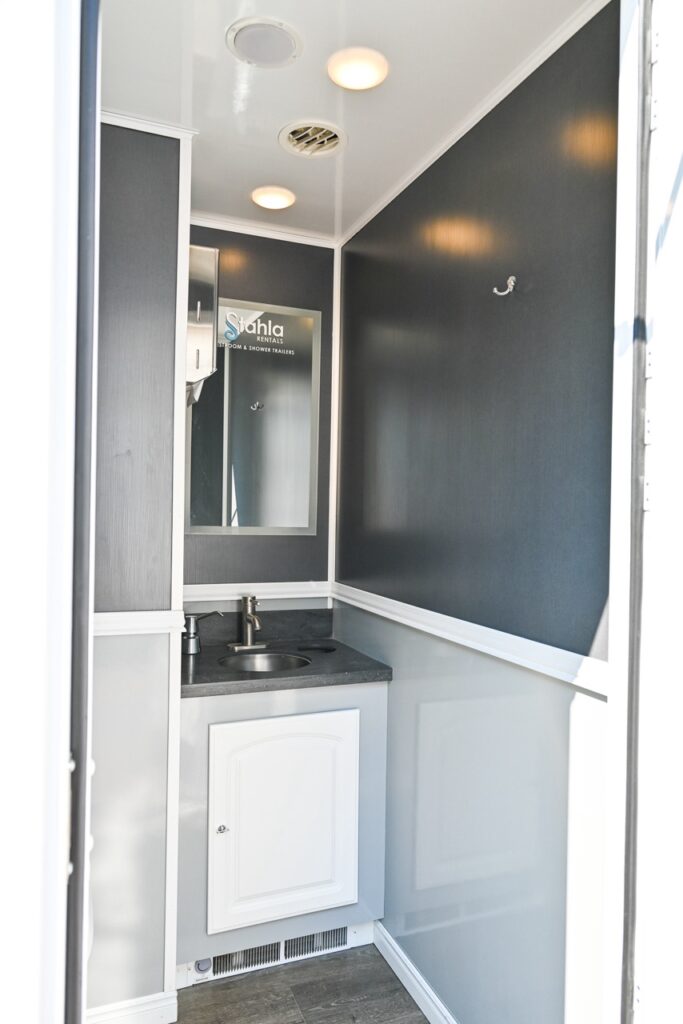 a small, modern bathroom by stahla services features a black countertop, white cabinets, a wall mounted mirror, and grey walls with white trim. there are ceiling lights and a small vent above the mirror, blending comfort and tradition.