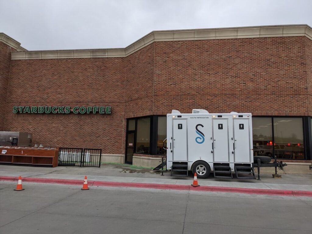 Image 6: exterior view of a starbucks coffee shop with a 4 stall restroom trailer rentals unit parked outside, marked with traffic cones.