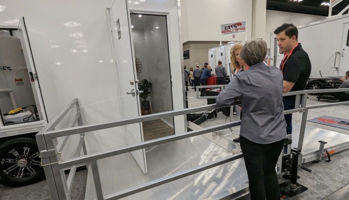 People at a trailer exhibit with portable restrooms.