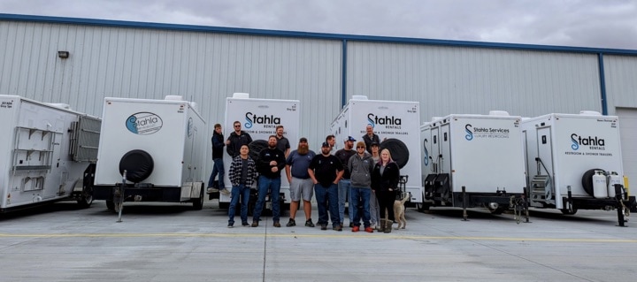 Team posing with portable restrooms outside warehouse.