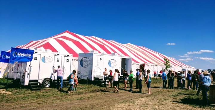 People at outdoor event near striped tent and trailers.