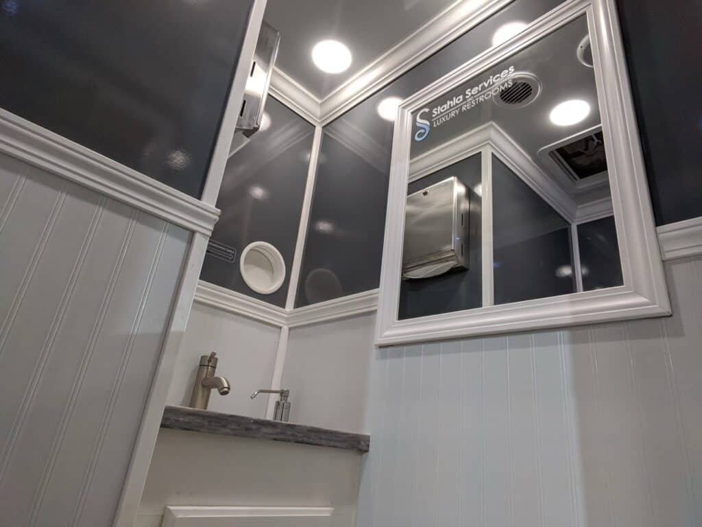 a small restroom interior with white and gray paneled walls, a rectangular mirror, small sink with a faucet, and ceiling lights above.