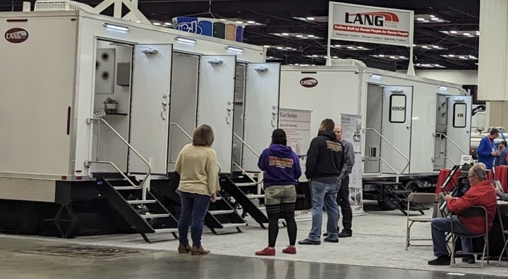People viewing portable restrooms at an expo.