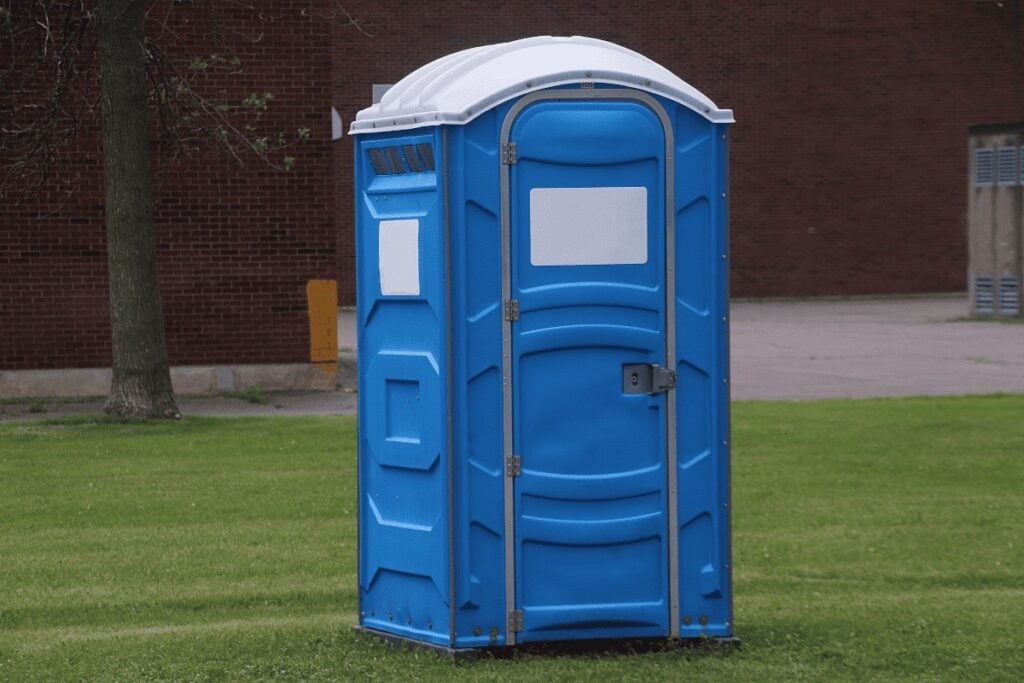 Portable blue toilet on grass near building.