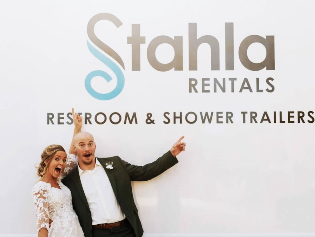 Excited couple posing by event rentals sign.