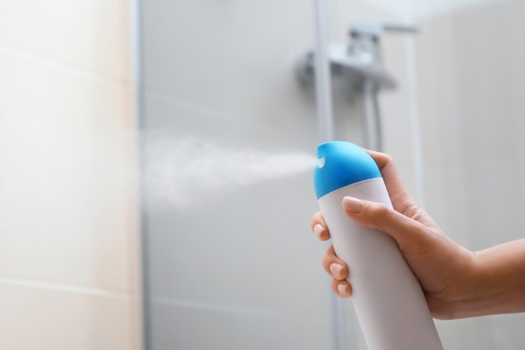 Hand spraying air freshener in bathroom.
