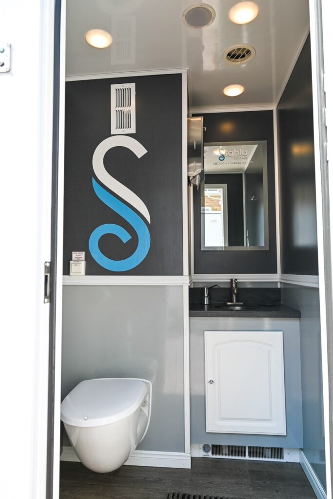 the image shows a clean restroom with a toilet, a sink, a mirror, and a decorative design on the wall featuring a blue and white swirl. the restroom has a modern, minimalistic appearance, showcasing the comfort and tradition one might expect during the orange city tulip festival.