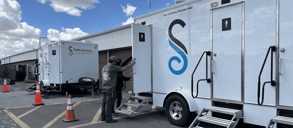 A technician works on mobile hygiene stations, such as restroom trailers parked outside a facility.